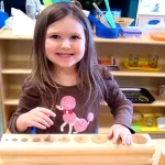 Skipwith Academy Stepping Stones Montessori - smiling girl learning with wooden shapes learning tool