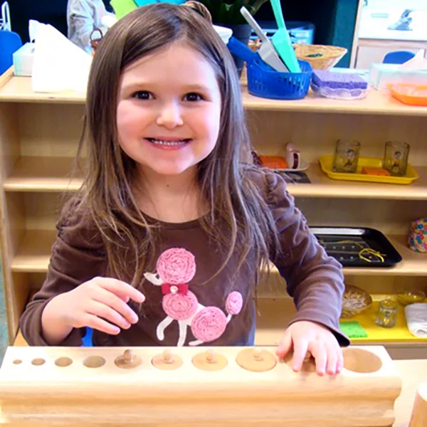 Skipwith Academy Stepping Stones Montessori - smiling girl learning with wooden shapes learning tool